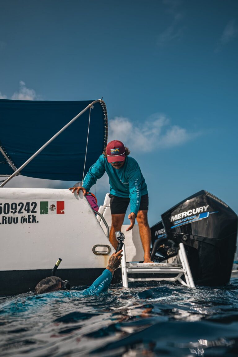 Guide handing a camera to a snorkeler at the stern ladder of the boat