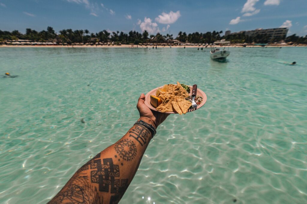 Plate of nachos, guacamole and ceviche held over turquoise water at Isla Mujeres beach